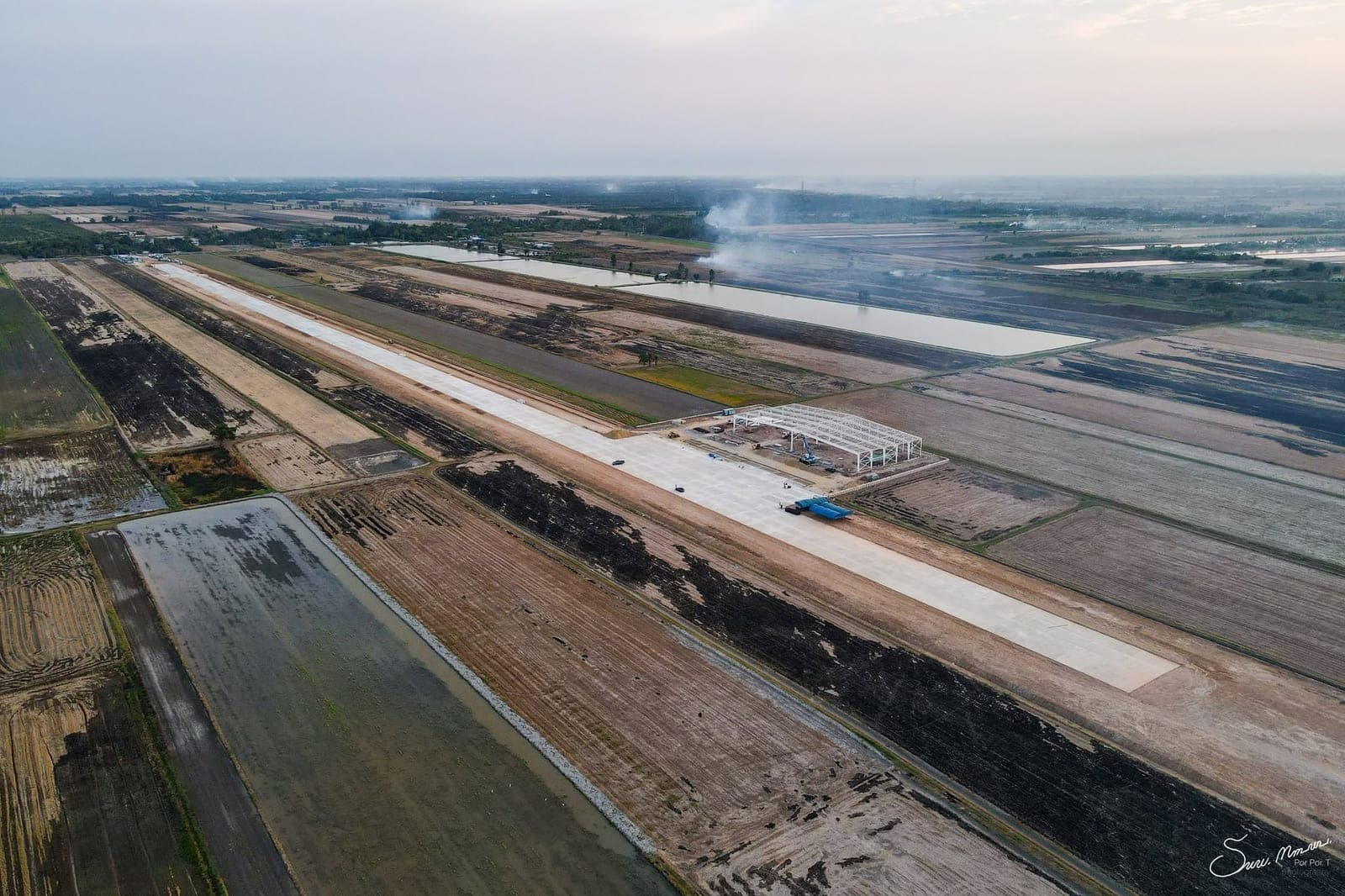Aerial view along the runway at dusk during construction, with the hangar frame beside the apron.